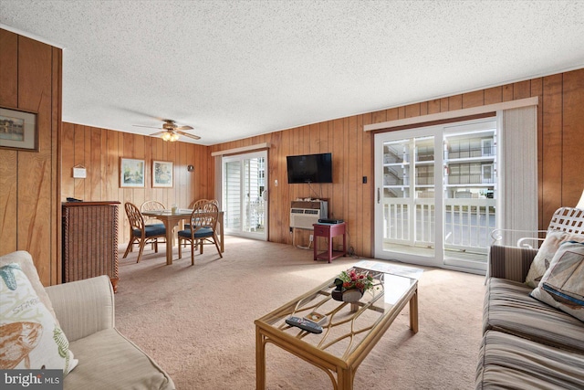 living room featuring wood walls, ceiling fan, light colored carpet, and a textured ceiling