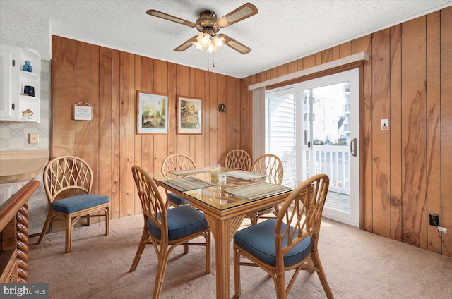 dining space featuring light carpet, wood walls, a textured ceiling, and ceiling fan