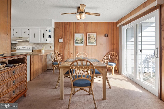 carpeted dining area with ceiling fan, a textured ceiling, and wooden walls