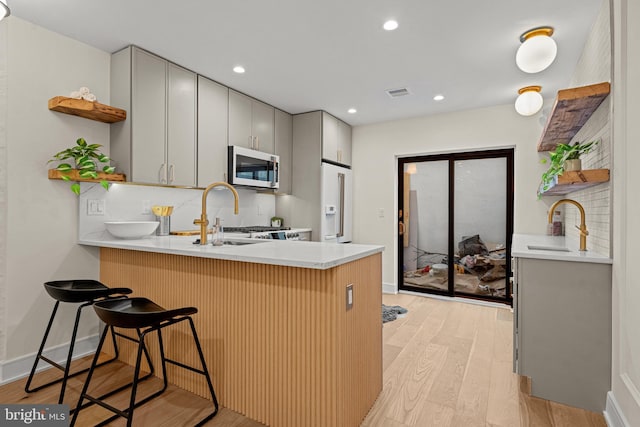 kitchen with a breakfast bar, backsplash, light wood-type flooring, and kitchen peninsula