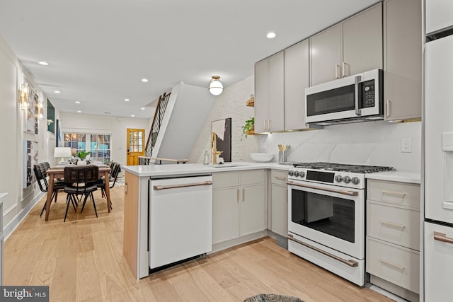 kitchen with sink, light hardwood / wood-style flooring, kitchen peninsula, and white appliances