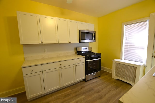 kitchen with radiator heating unit, hardwood / wood-style floors, light stone counters, white cabinetry, and stainless steel appliances