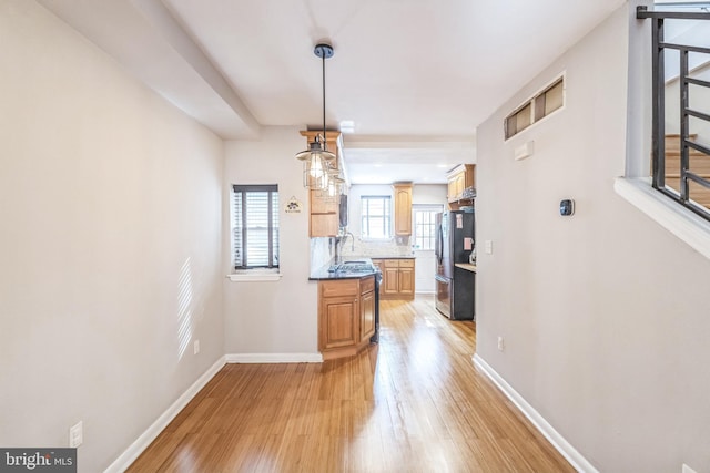 kitchen with tasteful backsplash, decorative light fixtures, light wood-type flooring, and stainless steel refrigerator