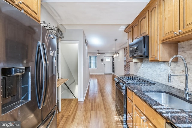 kitchen featuring hanging light fixtures, dark stone counters, light wood-type flooring, black appliances, and sink