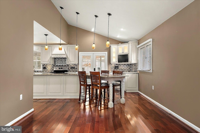 kitchen with white cabinetry, tasteful backsplash, dark hardwood / wood-style flooring, decorative light fixtures, and a breakfast bar area