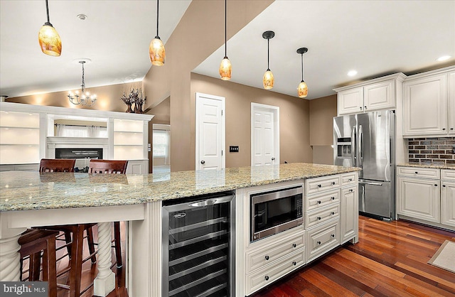 kitchen with appliances with stainless steel finishes, a kitchen breakfast bar, beverage cooler, white cabinets, and hanging light fixtures