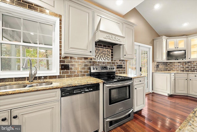 kitchen with premium range hood, white cabinets, sink, vaulted ceiling, and appliances with stainless steel finishes