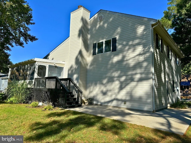 rear view of house featuring a lawn, a wooden deck, and a sunroom