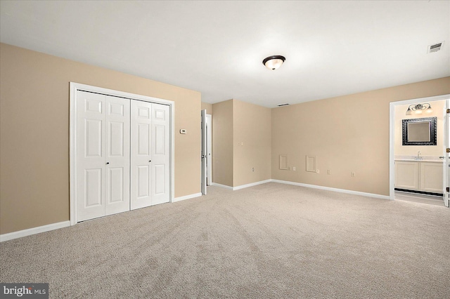 unfurnished bedroom featuring light colored carpet, ensuite bath, a closet, and sink