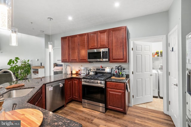 kitchen featuring appliances with stainless steel finishes, hanging light fixtures, hardwood / wood-style floors, sink, and washer and dryer