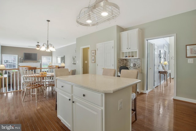 kitchen featuring a kitchen island, hanging light fixtures, a kitchen breakfast bar, white cabinets, and dark wood-type flooring