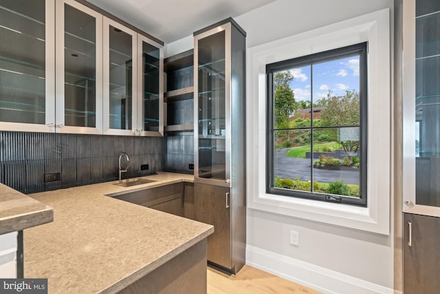 bar with light wood-type flooring, tasteful backsplash, baseboards, and a sink