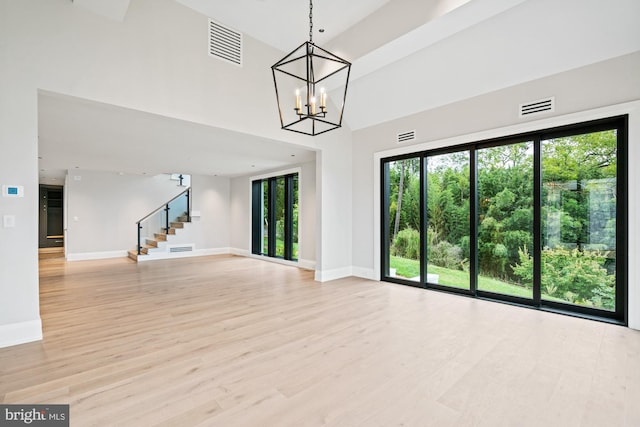 unfurnished living room with light wood-type flooring, visible vents, an inviting chandelier, and stairs