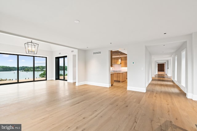 unfurnished living room featuring light wood finished floors, visible vents, baseboards, a water view, and an inviting chandelier