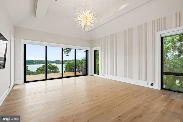 empty room featuring wood finished floors, baseboards, an inviting chandelier, lofted ceiling, and a water view