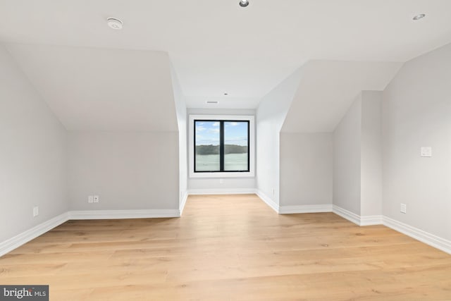 bonus room with vaulted ceiling, light wood-style flooring, and baseboards