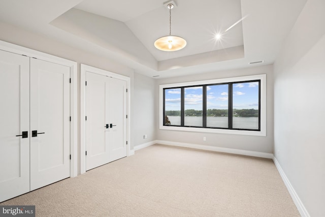 unfurnished bedroom with carpet flooring, two closets, a raised ceiling, and baseboards