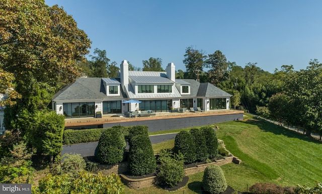 back of property featuring a standing seam roof, a lawn, a chimney, and metal roof