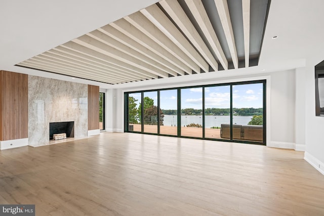 unfurnished living room with baseboards, a water view, wood finished floors, and a high end fireplace