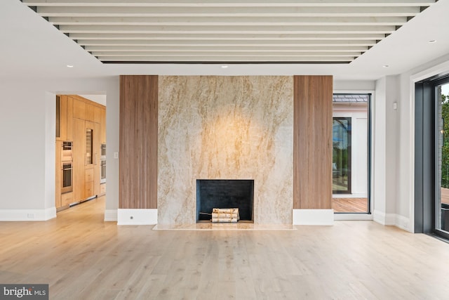 unfurnished living room featuring baseboards, beam ceiling, wood finished floors, and a high end fireplace