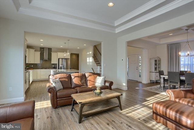 living room featuring a raised ceiling, ornamental molding, and light wood-type flooring