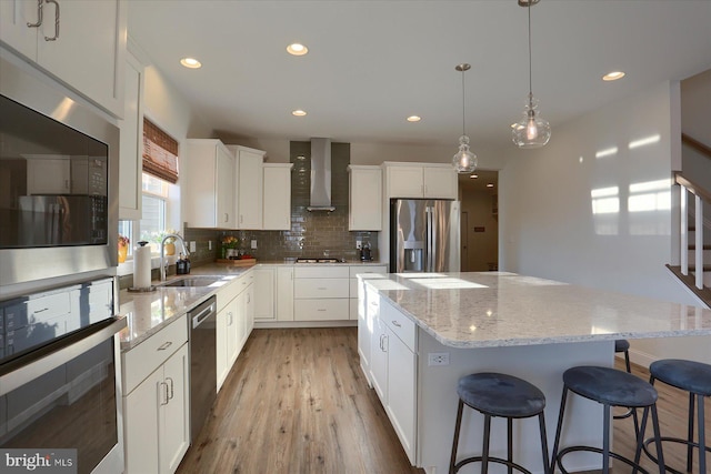 kitchen with wall chimney range hood, appliances with stainless steel finishes, sink, a center island, and hanging light fixtures