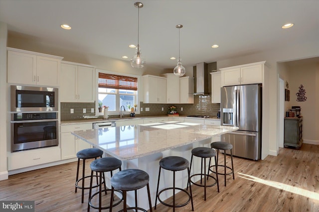 kitchen with appliances with stainless steel finishes, white cabinetry, light hardwood / wood-style floors, wall chimney exhaust hood, and a center island