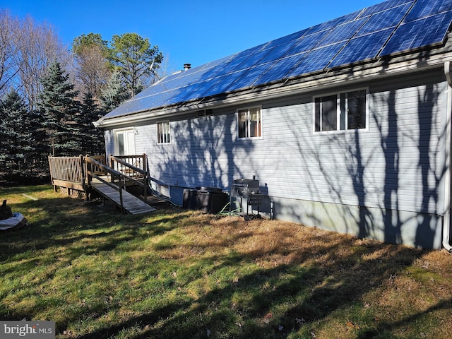 rear view of house featuring a deck, a lawn, and solar panels