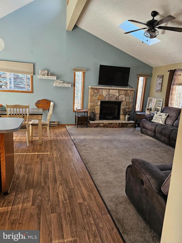 living room with lofted ceiling with beams, dark wood-type flooring, a stone fireplace, and ceiling fan