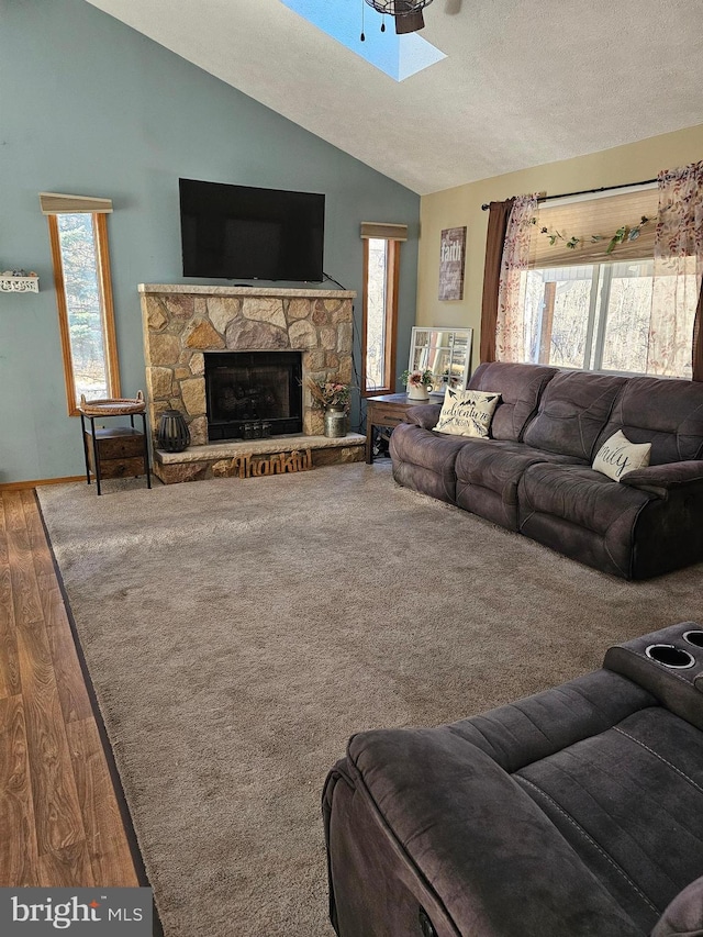 living room featuring a stone fireplace, lofted ceiling, a healthy amount of sunlight, and wood-type flooring