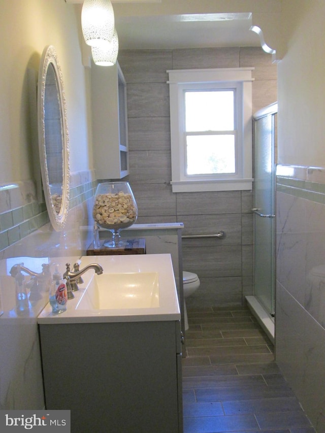 bathroom featuring toilet, a shower with shower door, wood-type flooring, vanity, and tile walls