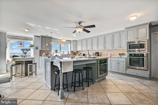 kitchen with gray cabinetry, a center island, light stone countertops, light tile patterned floors, and stainless steel appliances