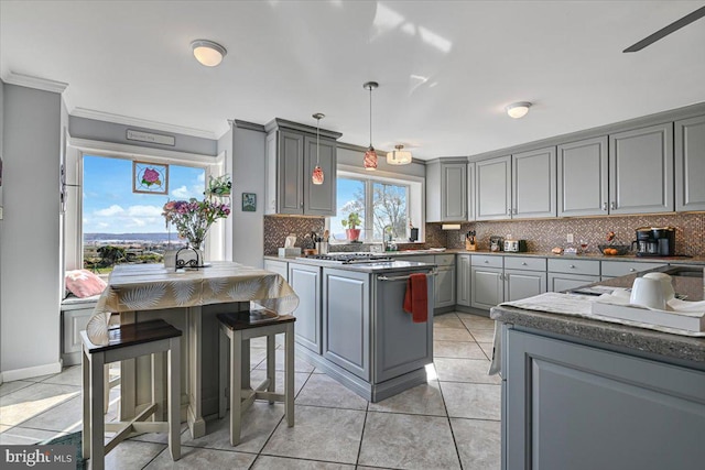 kitchen featuring backsplash, ornamental molding, gray cabinetry, hanging light fixtures, and light tile patterned flooring