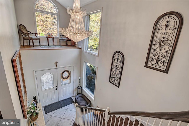 foyer featuring light tile patterned floors, a towering ceiling, an inviting chandelier, and plenty of natural light