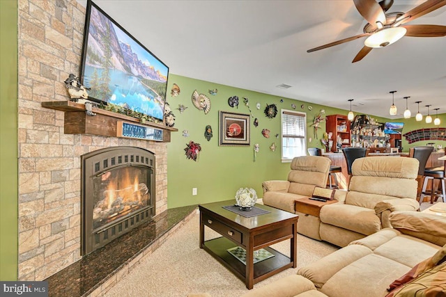 living room with ceiling fan, a stone fireplace, and light colored carpet