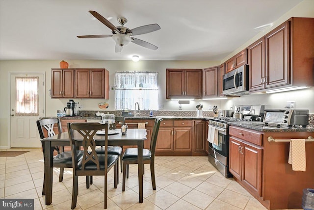 kitchen with sink, ceiling fan, dark stone countertops, light tile patterned floors, and appliances with stainless steel finishes