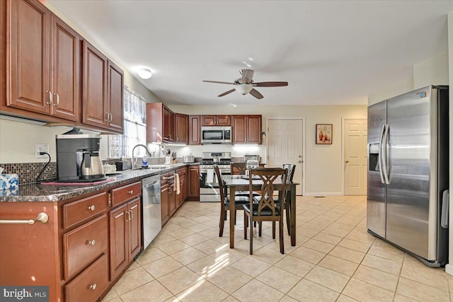 kitchen with ceiling fan, sink, stainless steel appliances, dark stone counters, and light tile patterned floors