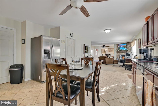 tiled dining space with ceiling fan and a stone fireplace