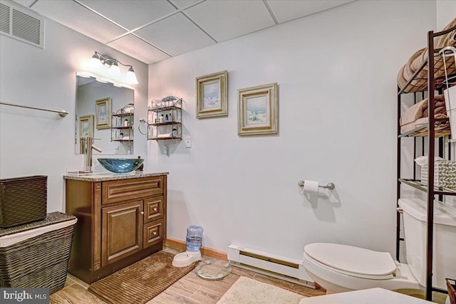 bathroom with a paneled ceiling, vanity, a baseboard radiator, hardwood / wood-style flooring, and toilet