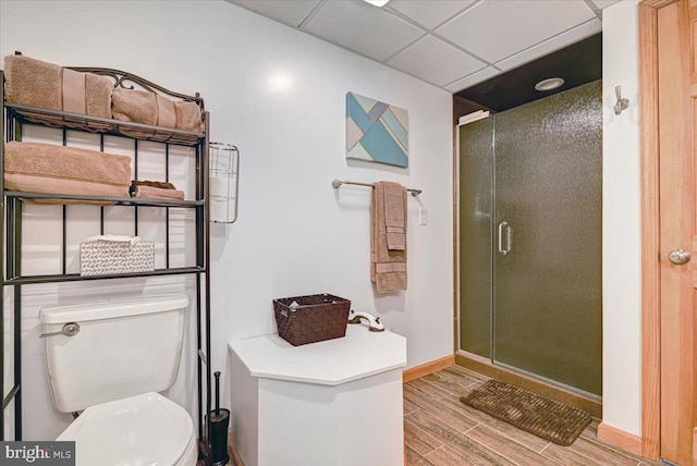 bathroom featuring a paneled ceiling, hardwood / wood-style floors, a shower with shower door, and toilet