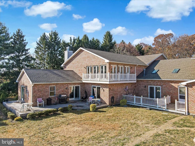 rear view of property featuring a lawn, a patio area, a balcony, and french doors