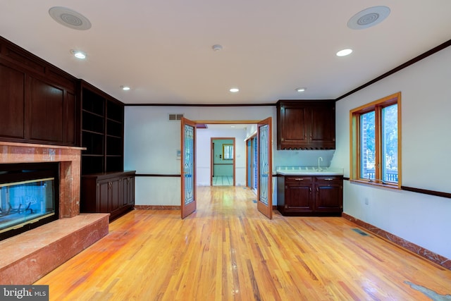 kitchen with dark brown cabinets, a high end fireplace, light wood-type flooring, crown molding, and sink