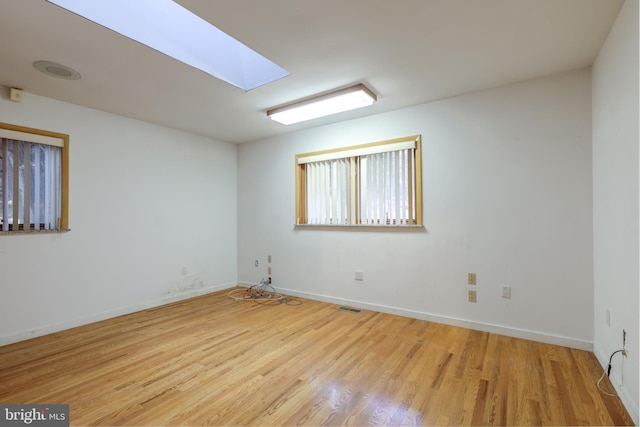 empty room featuring a skylight and light wood-type flooring