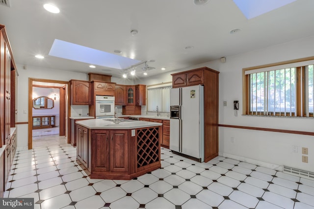 kitchen featuring white fridge with ice dispenser, a kitchen island with sink, sink, and a skylight