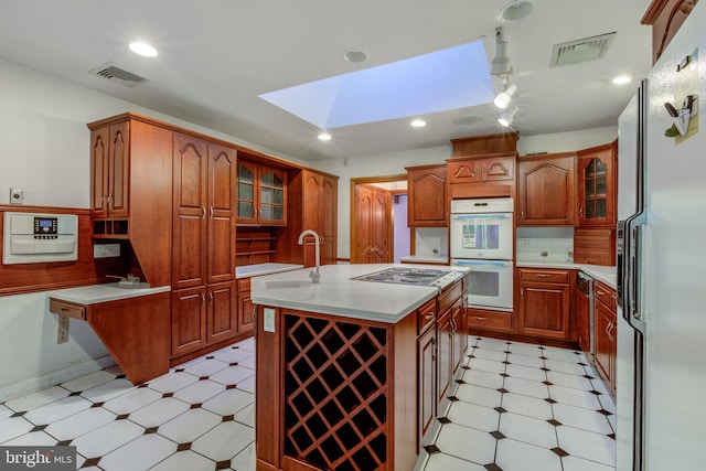 kitchen with decorative backsplash, a kitchen island with sink, sink, white appliances, and a skylight