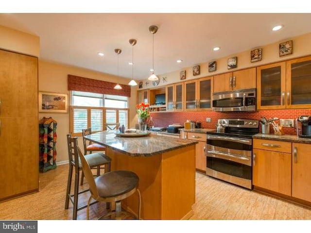 kitchen with pendant lighting, a center island, stainless steel appliances, and dark stone counters