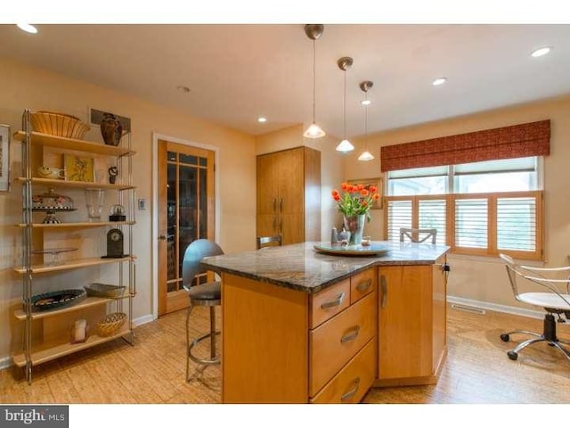 kitchen featuring dark stone countertops, light hardwood / wood-style floors, a center island, and decorative light fixtures