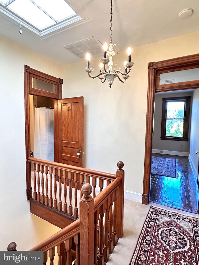 corridor featuring light carpet, a notable chandelier, and a skylight