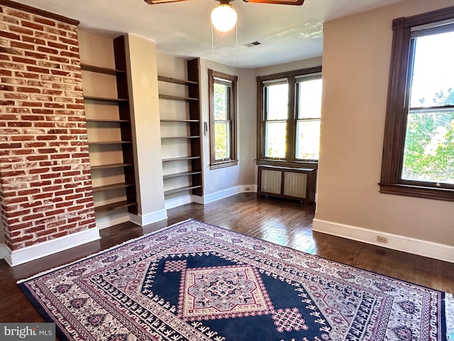 interior space with ceiling fan, visible vents, dark wood-style floors, baseboards, and radiator heating unit