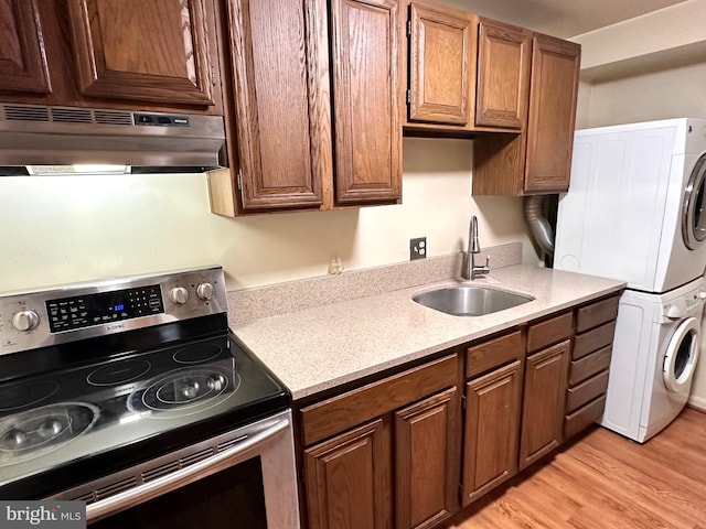 kitchen with stacked washer / drying machine, sink, light wood-type flooring, and electric stove